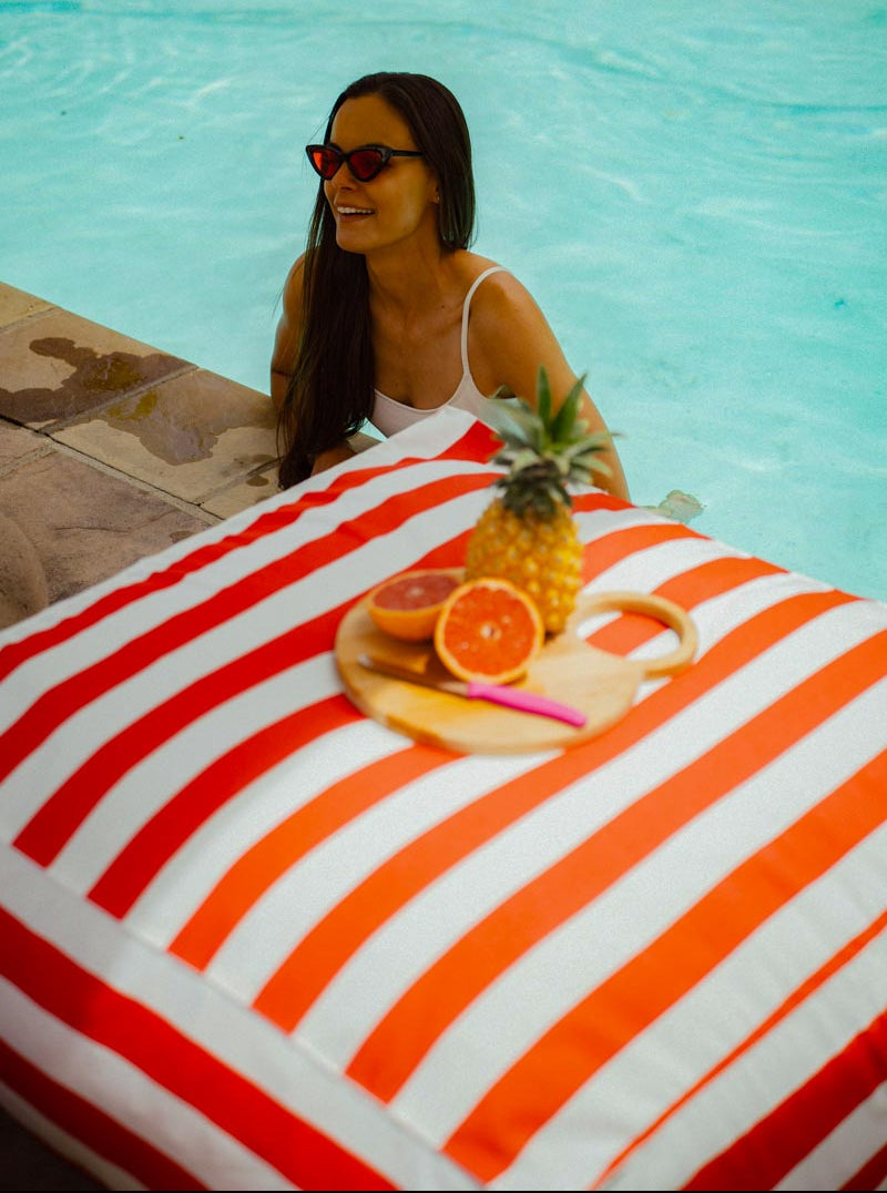 Woman by a pool with a striped towel, pineapple, and oranges.