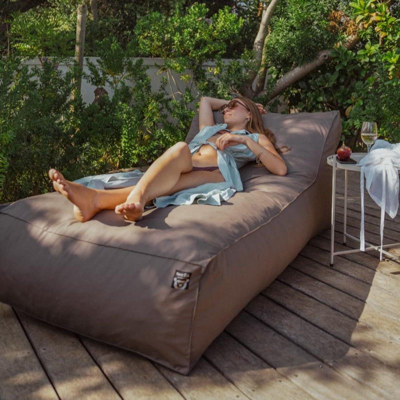 Person relaxing on a large outdoor bean bag chair in a garden setting.