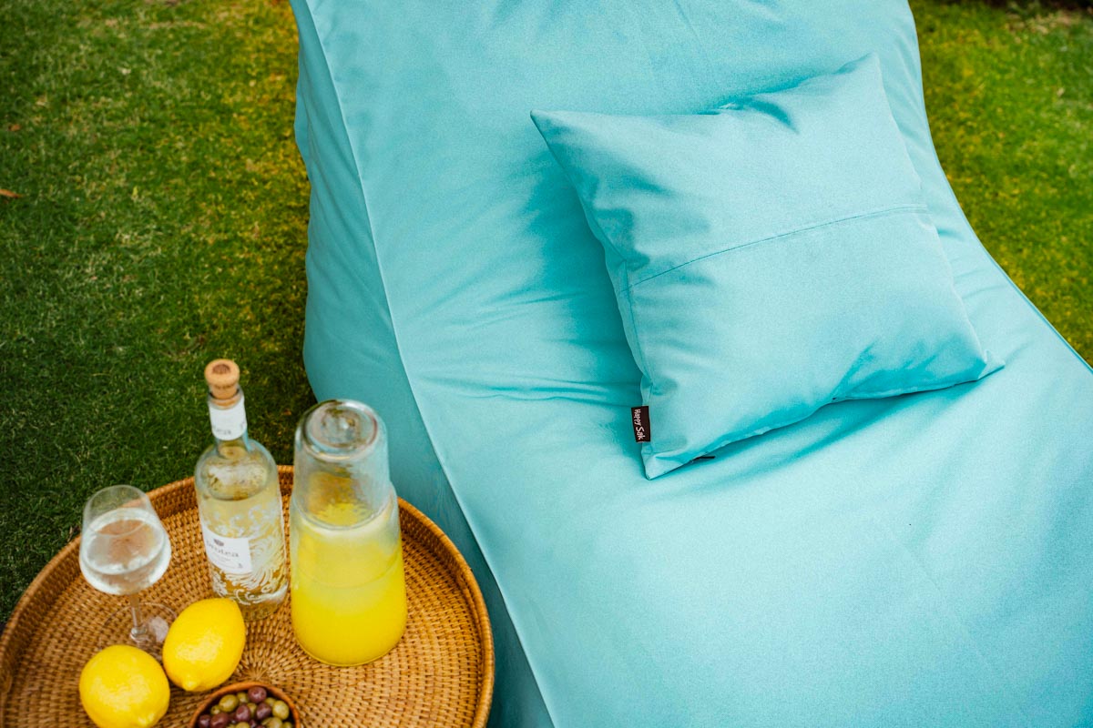 Turquoise bean bag chair with a small table holding drinks and lemons on a grassy background