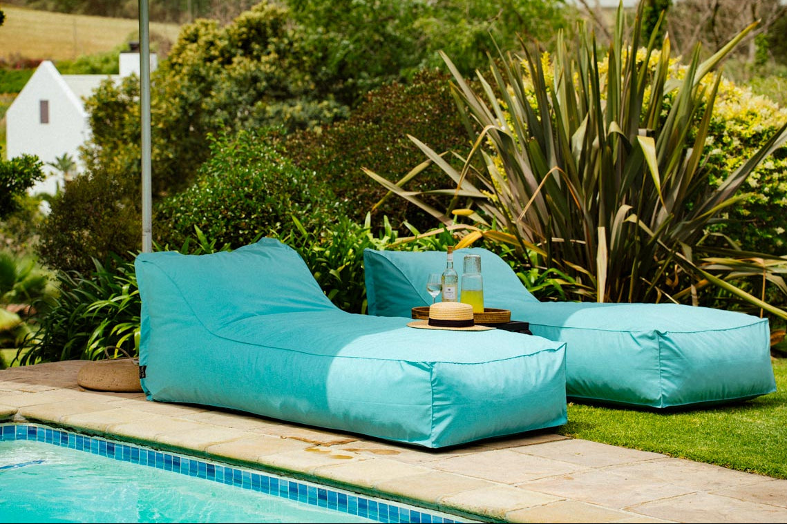 Turquoise bean bag chairs by a pool with plants in the background