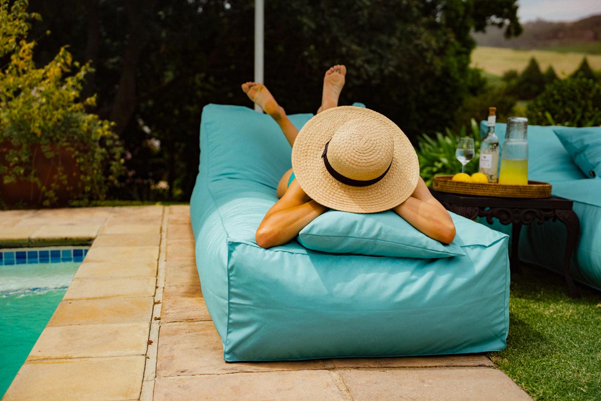 Person relaxing on a blue lounge chair by a poolside with a scenic background