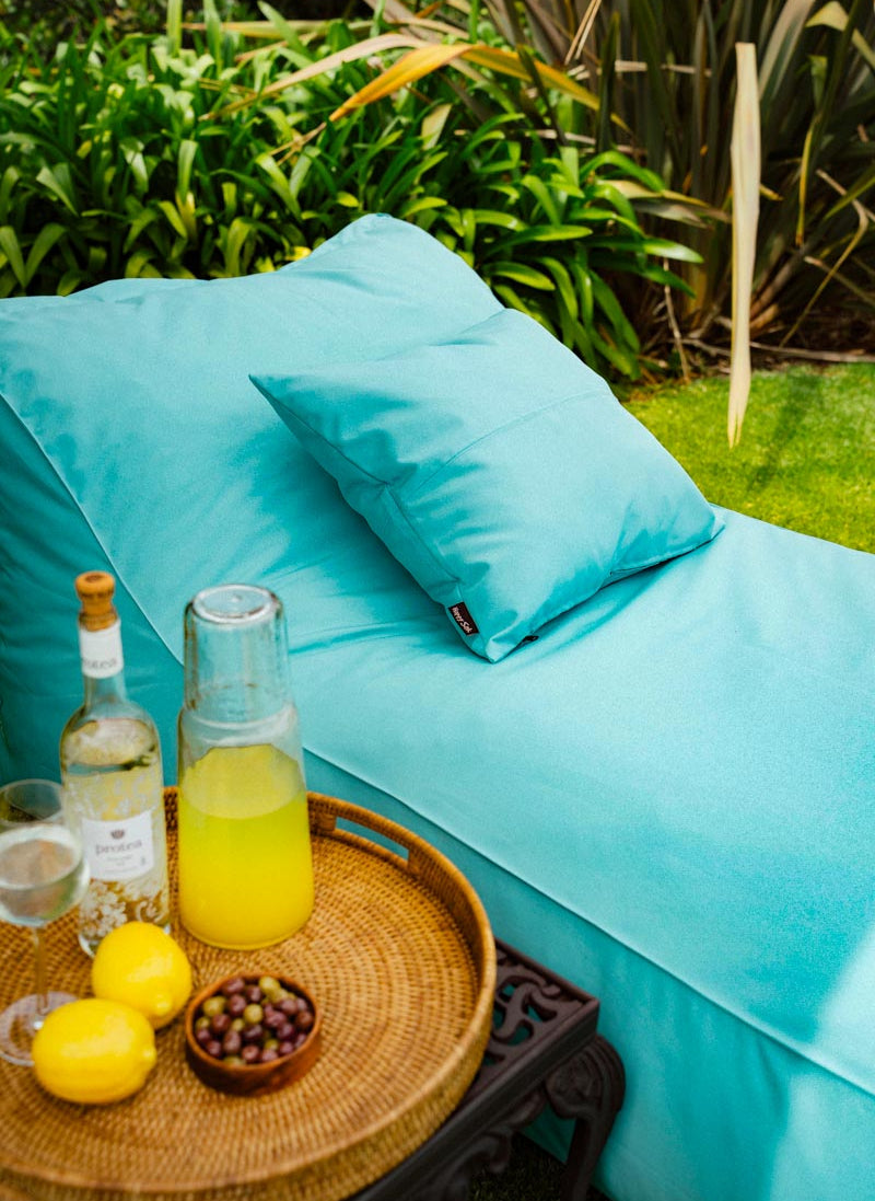 Turquoise outdoor cushions on a bench with a small table holding lemons, a bottle, and a pitcher.