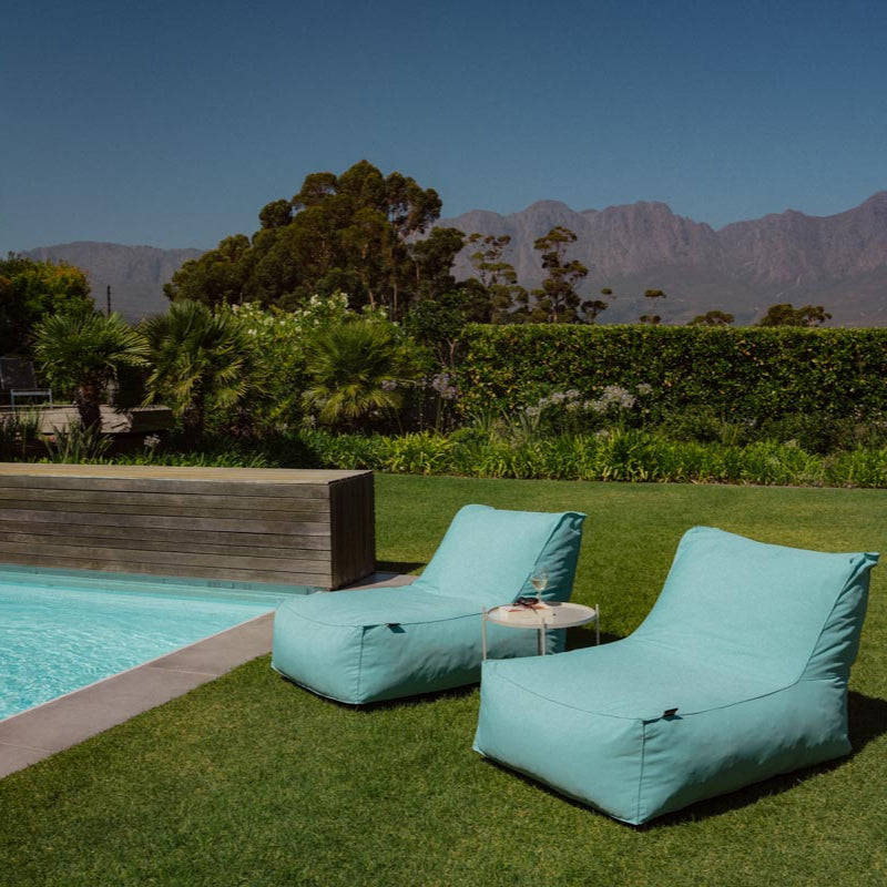 Turquoise lounge chairs by a pool with mountains in the background