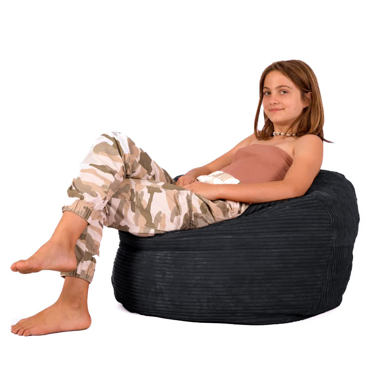 A child sitting on a black corduroy Footsak bean bag chair with their feet up on a matching foot rest.