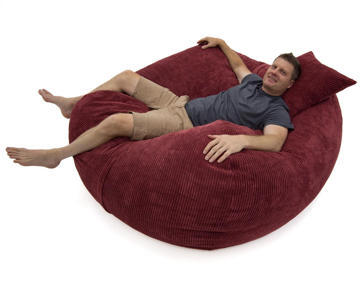 Man lying on a large red bean bag chair against a white background