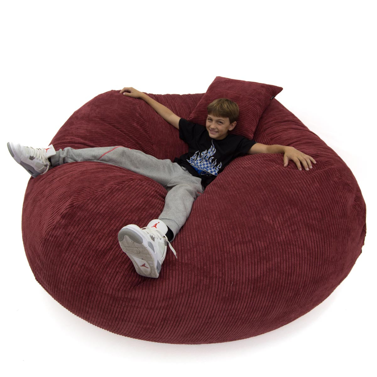 Child sitting on a large red bean bag chair against a white background