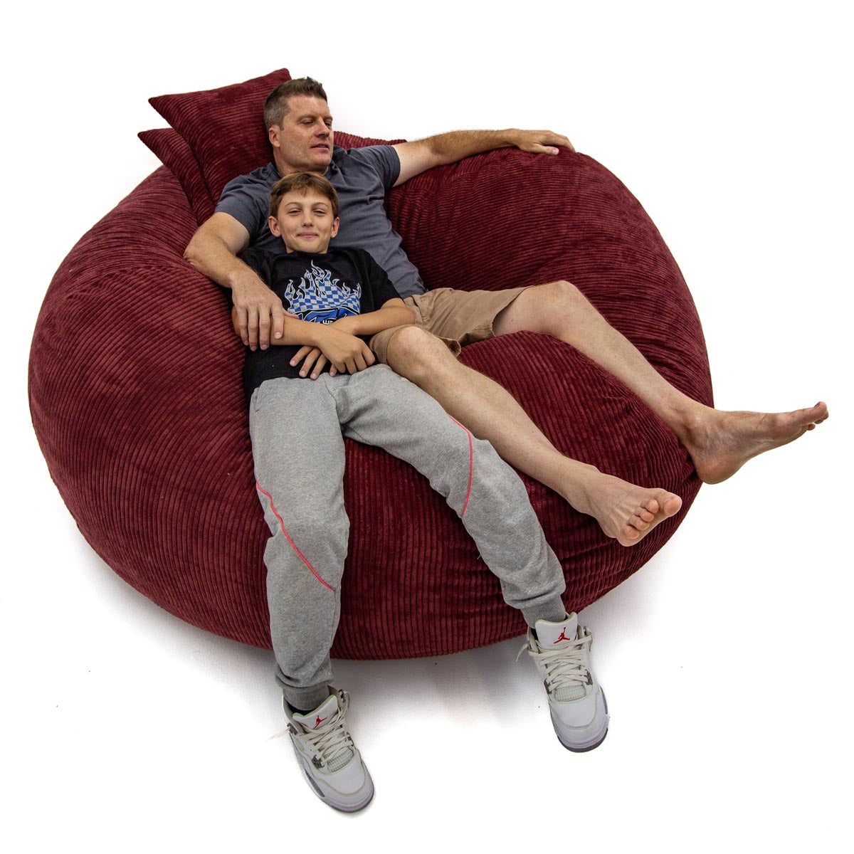 Two people sitting on a large red bean bag chair against a white background