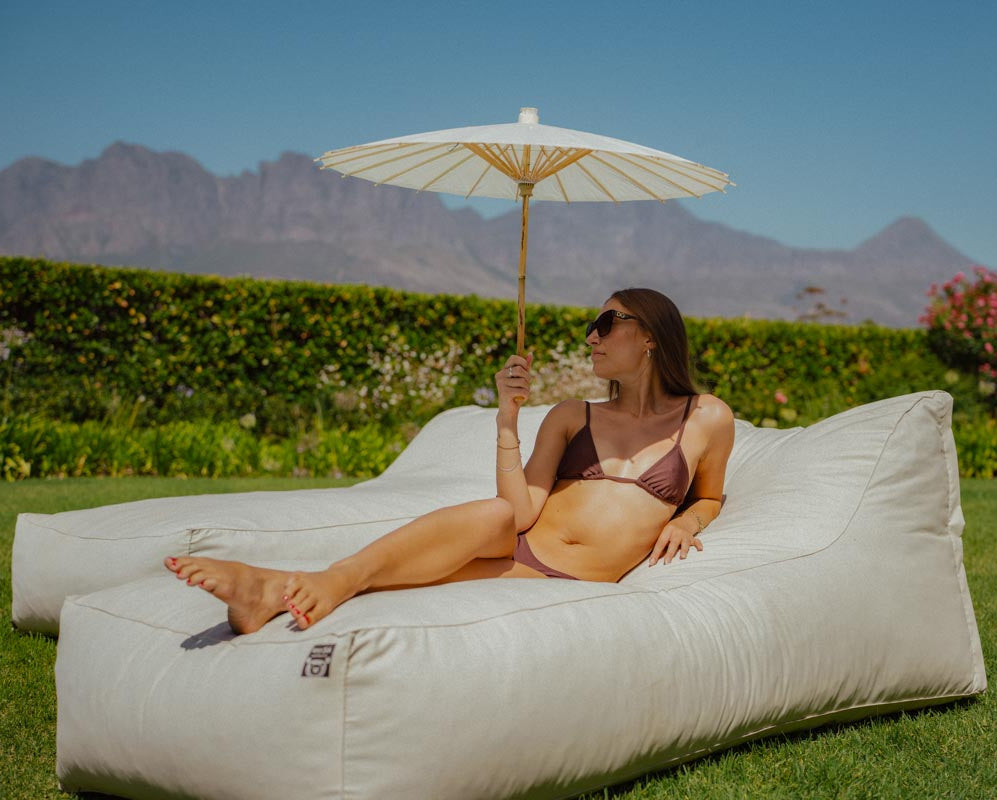 Woman relaxing on a bean bag chair with an umbrella in a scenic outdoor setting