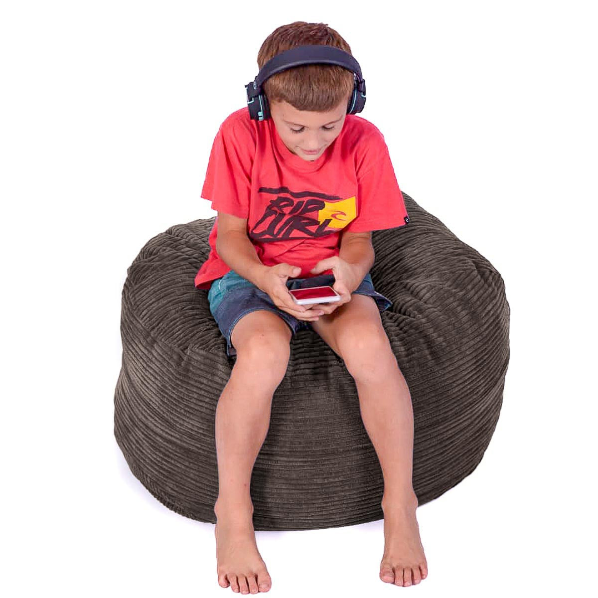 Child sitting on a bean bag chair wearing headphones and holding a phone.