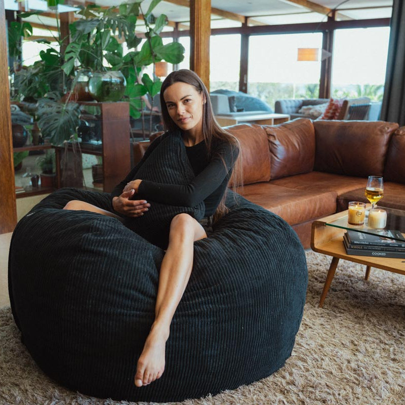 Woman sitting on a black bean bag chair in a modern living room.