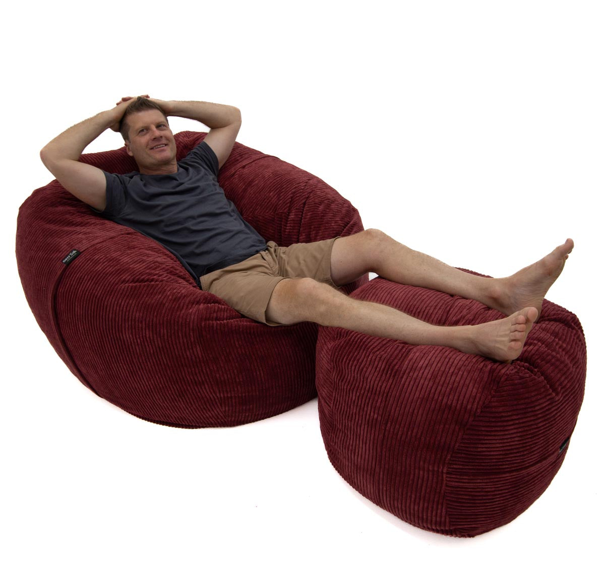 Man relaxing on a large red bean bag chair against a white background