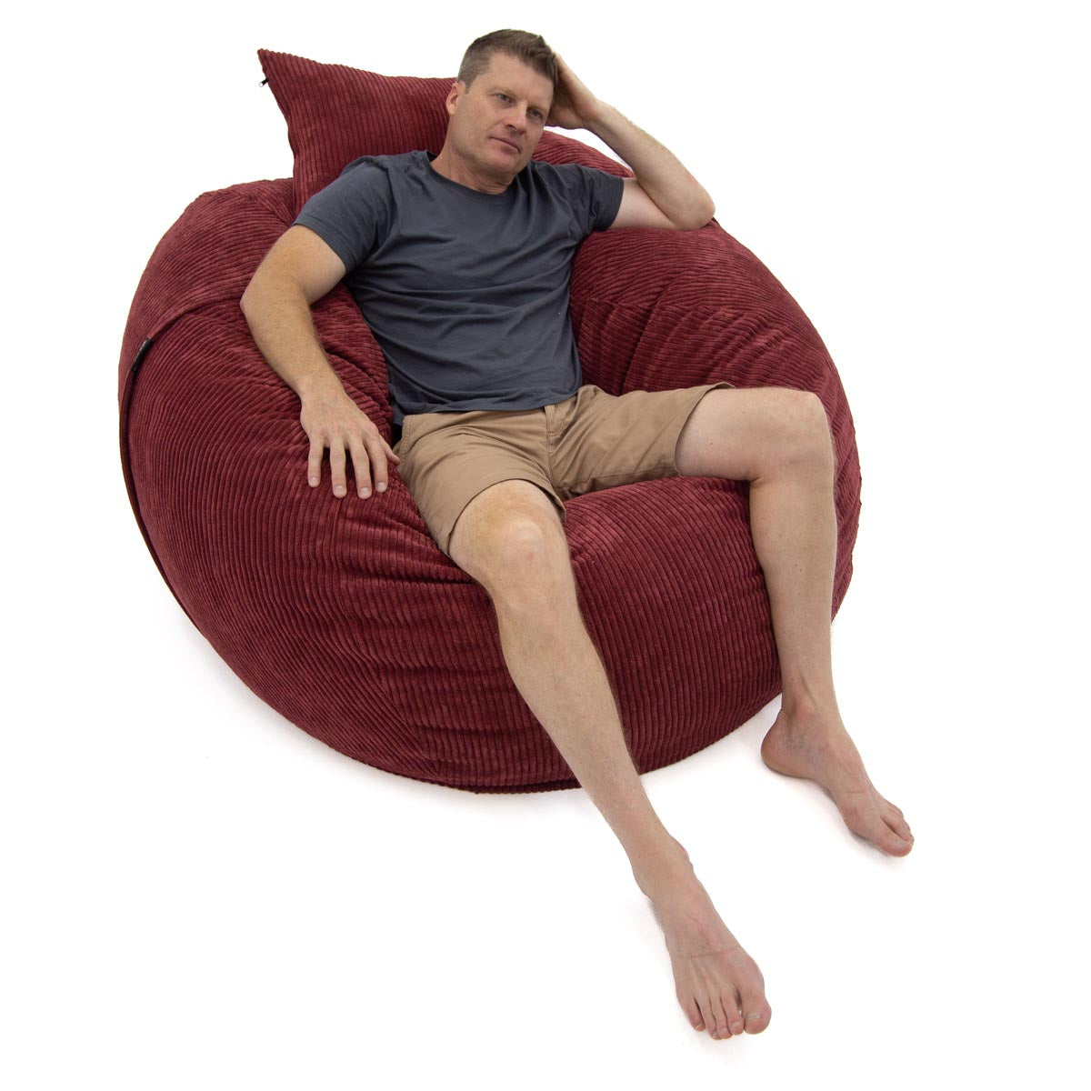 Man relaxing on a large red bean bag chair against a white background