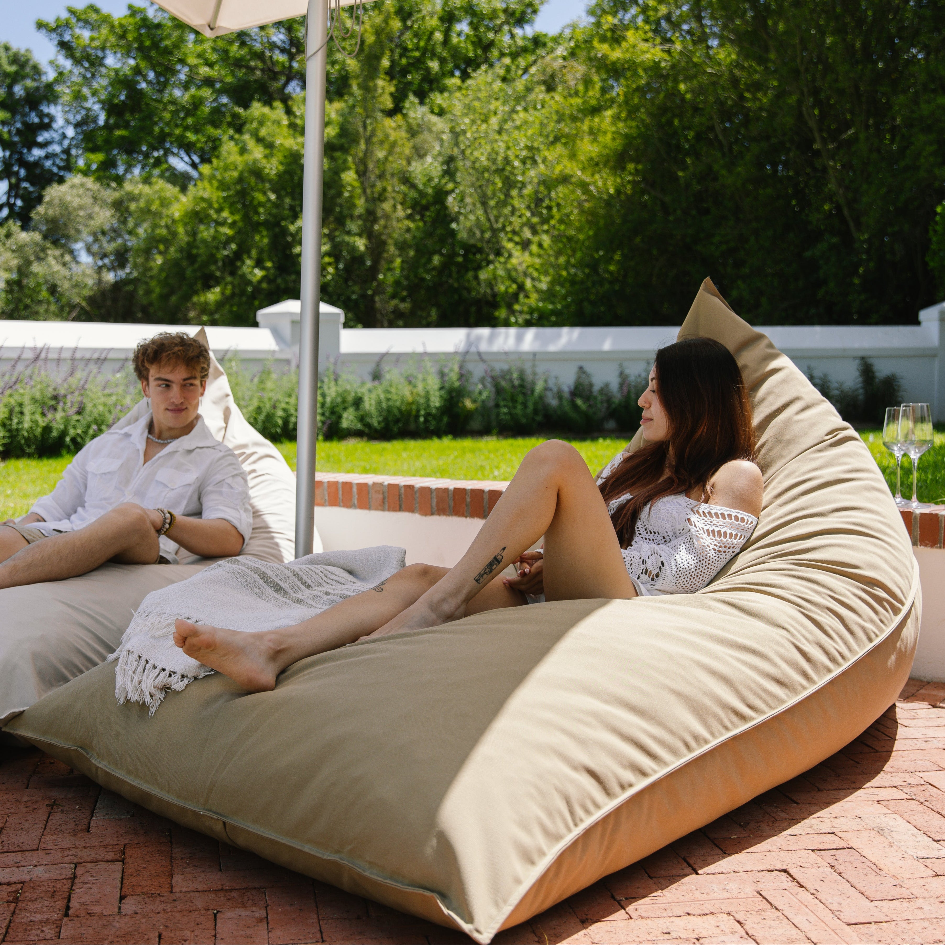Two people relaxing on large beige bean bag chairs outdoors.
