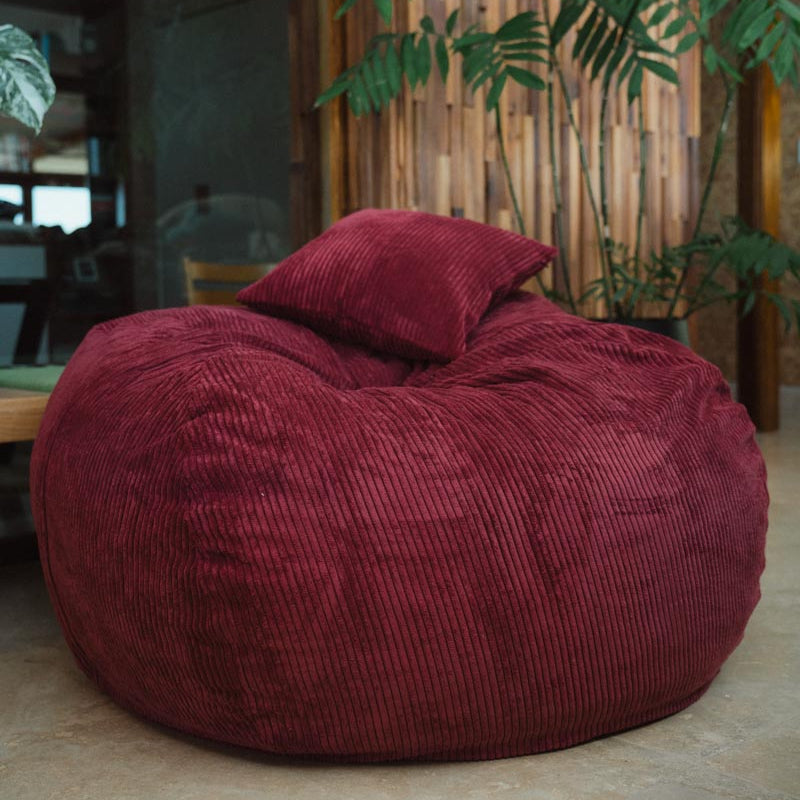 Maroon bean bag chair with a pillow in a room with plants and wooden furniture.