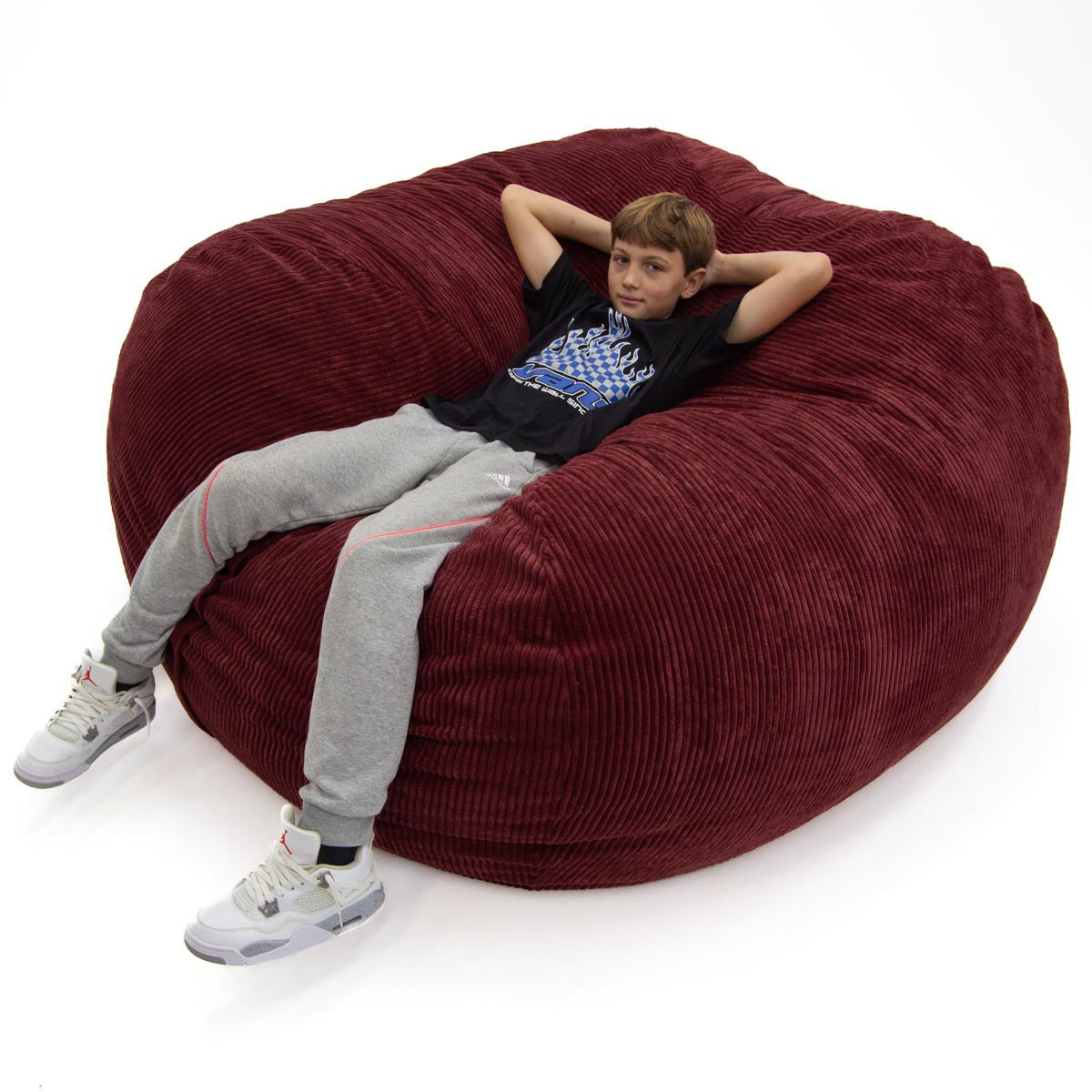 Child sitting on a large red bean bag chair against a white background