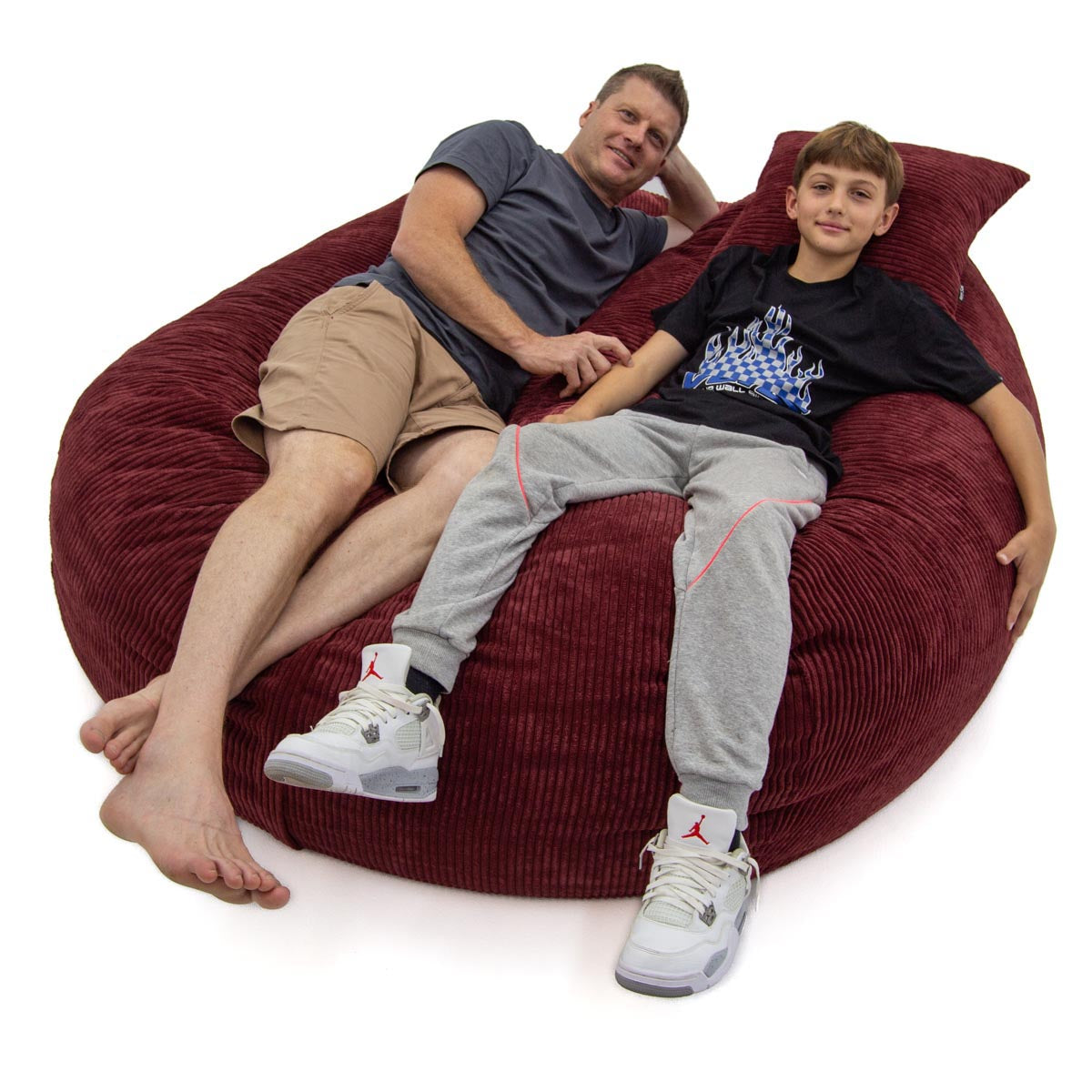 Two people sitting on a large red bean bag chair against a white background