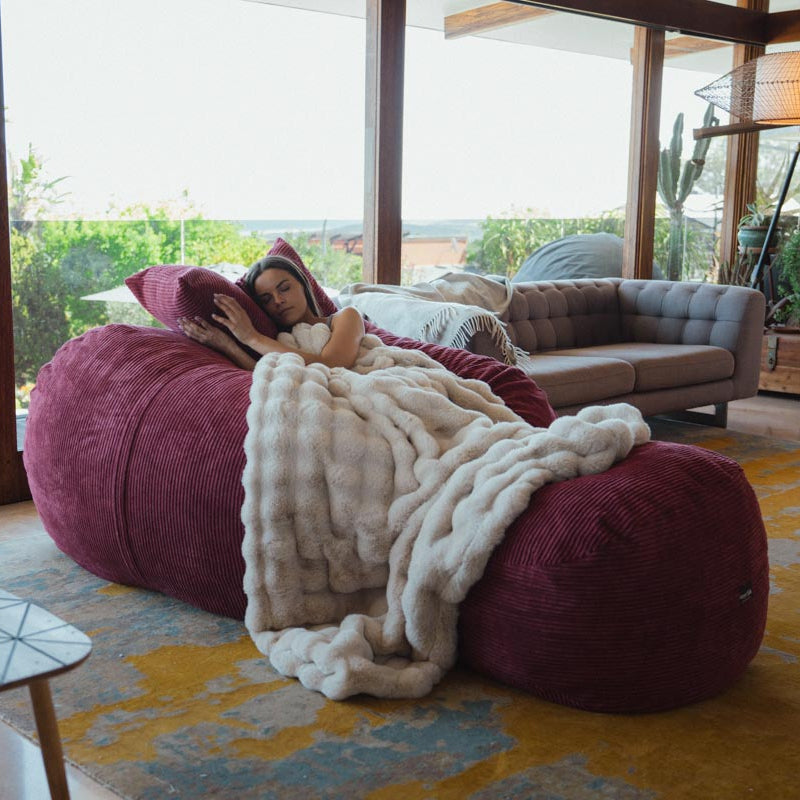 Person lying on a large bean bag with a blanket in a modern living room.