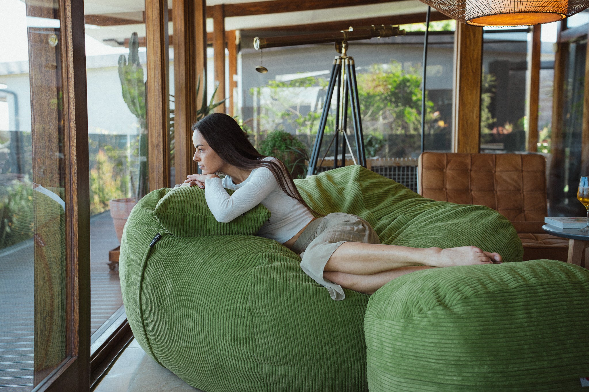 Woman sitting on a green bean bag chair in a modern indoor setting with large windows.
