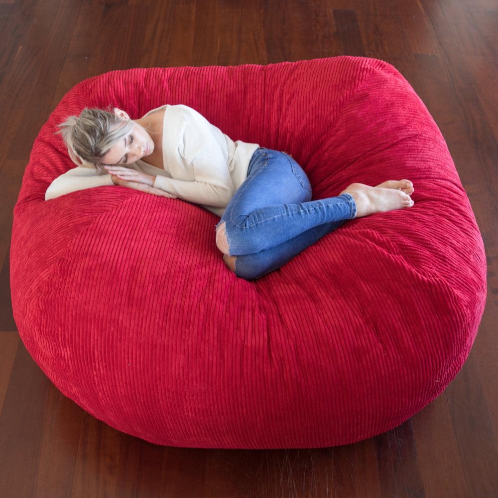 A person lounging on a large red corduroy bean bag chair.