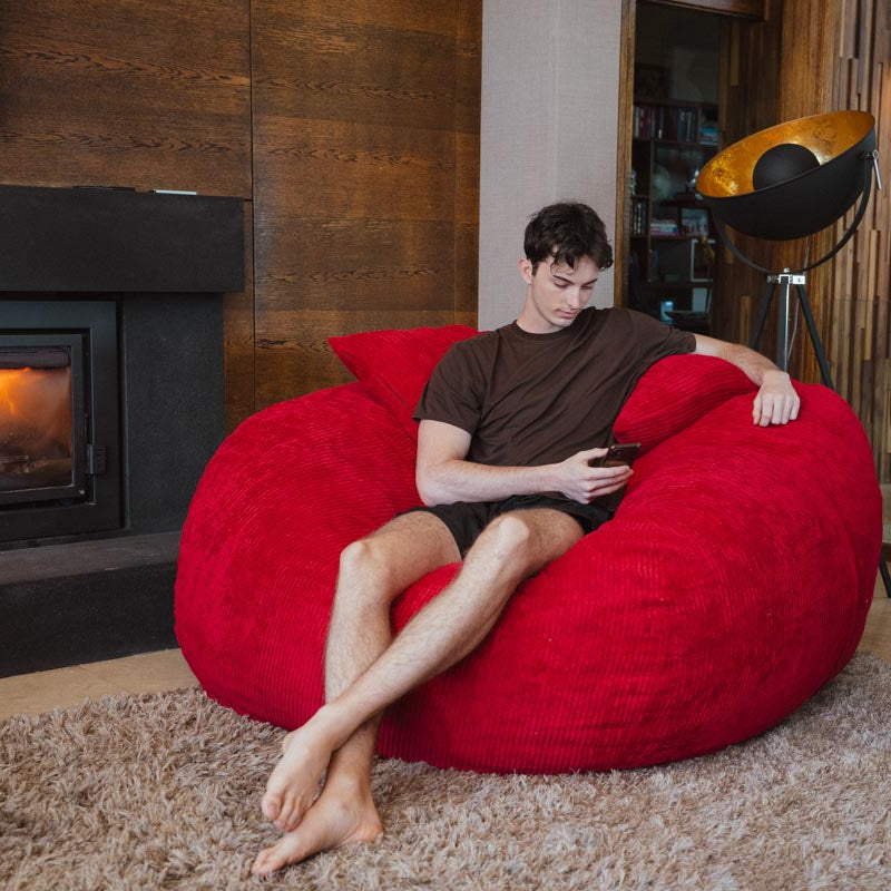 Person sitting on a red bean bag chair in a cozy living room with a fireplace.