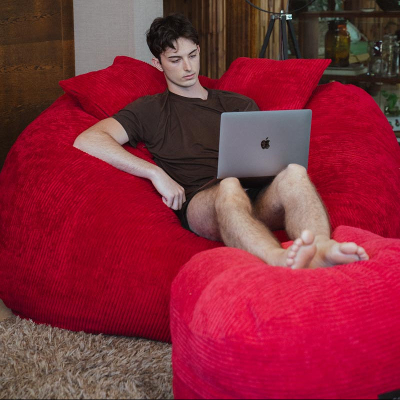 Person using a laptop on a red bean bag chair in a cozy room.