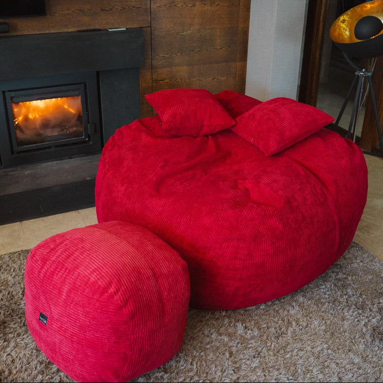Red bean bag chair in a living room with a fireplace and decorative items.