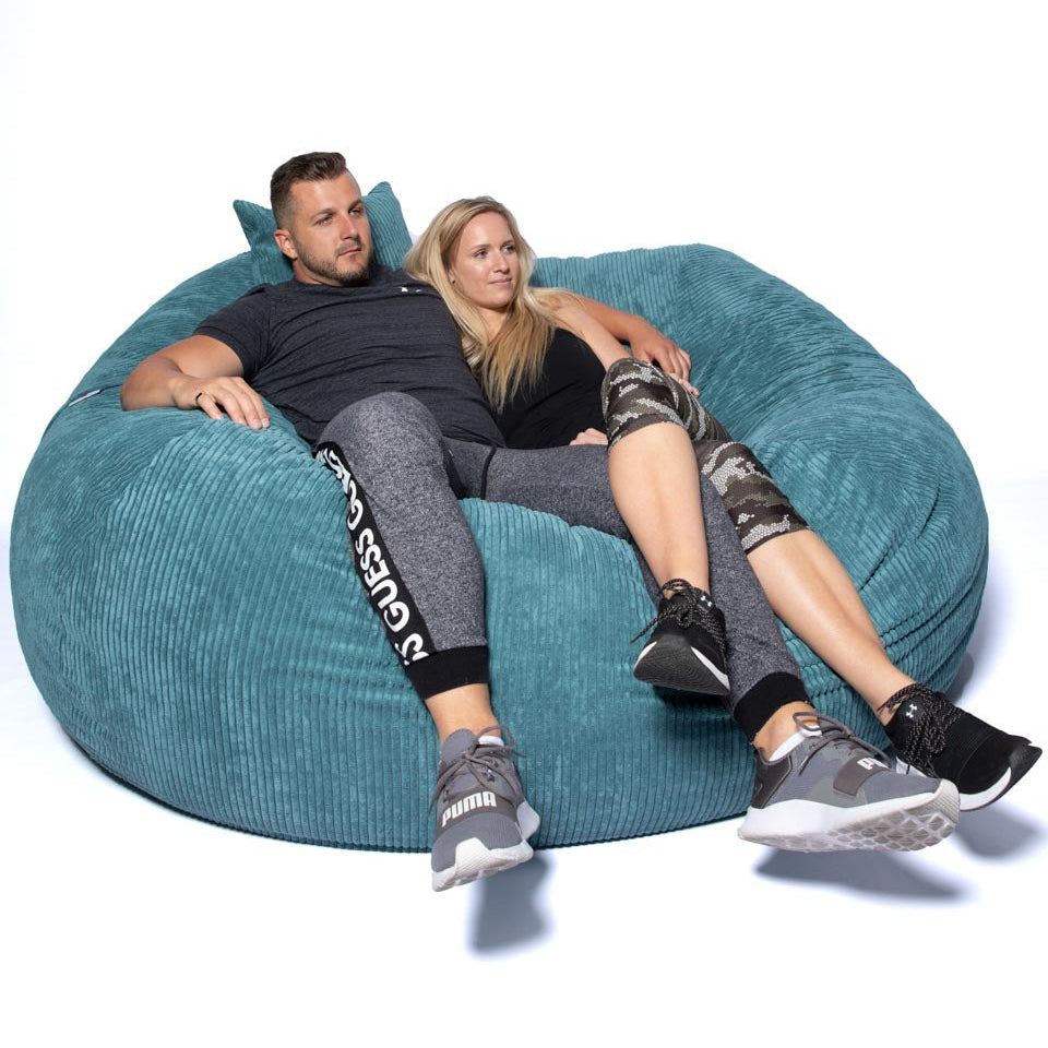 Two people sitting on a large teal bean bag chair against a white background