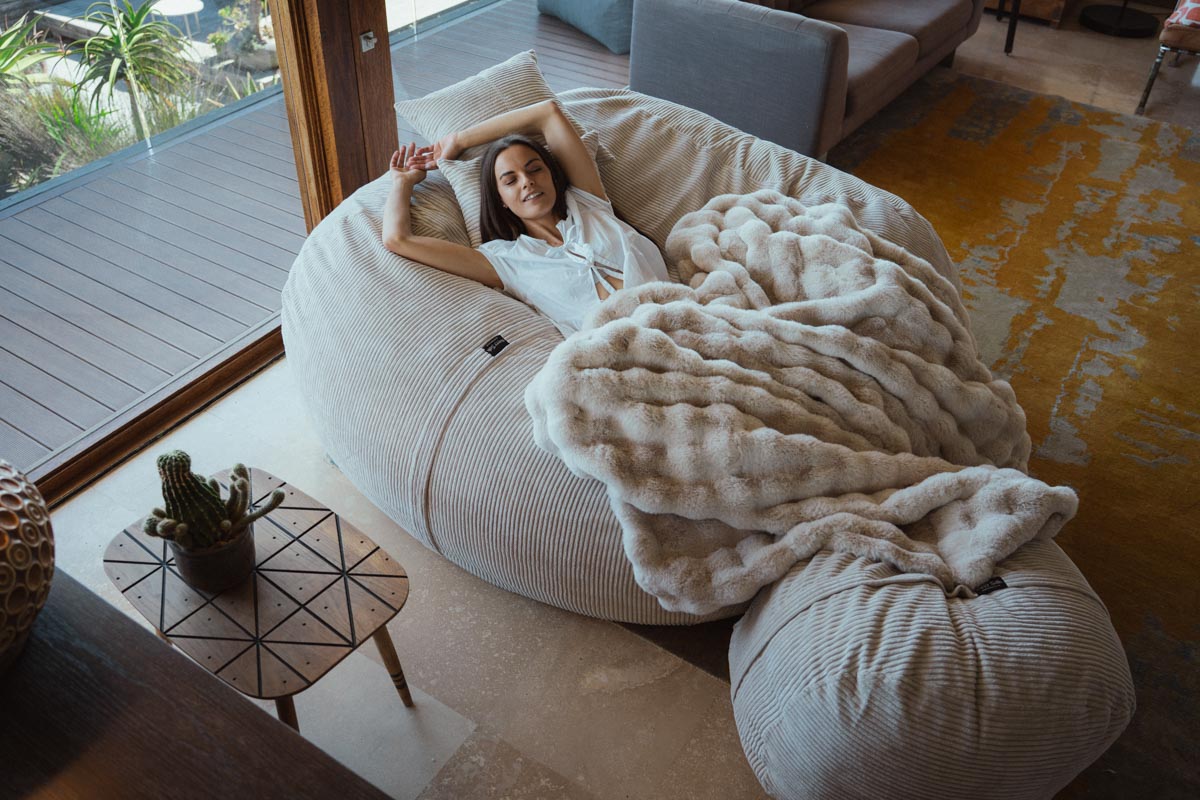 Woman lying on a large, fluffy white bean bag chair in a modern living room.