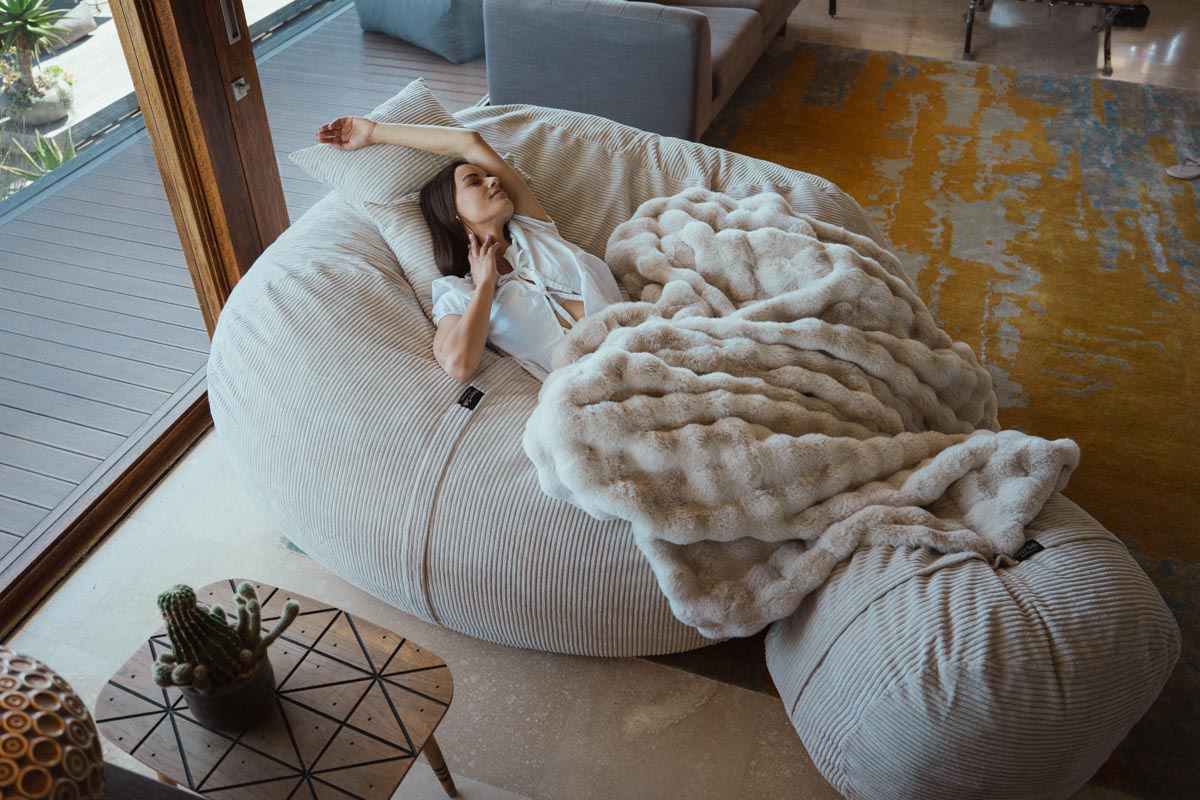 Woman relaxing on a large bean bag chair with a blanket in a modern living room.