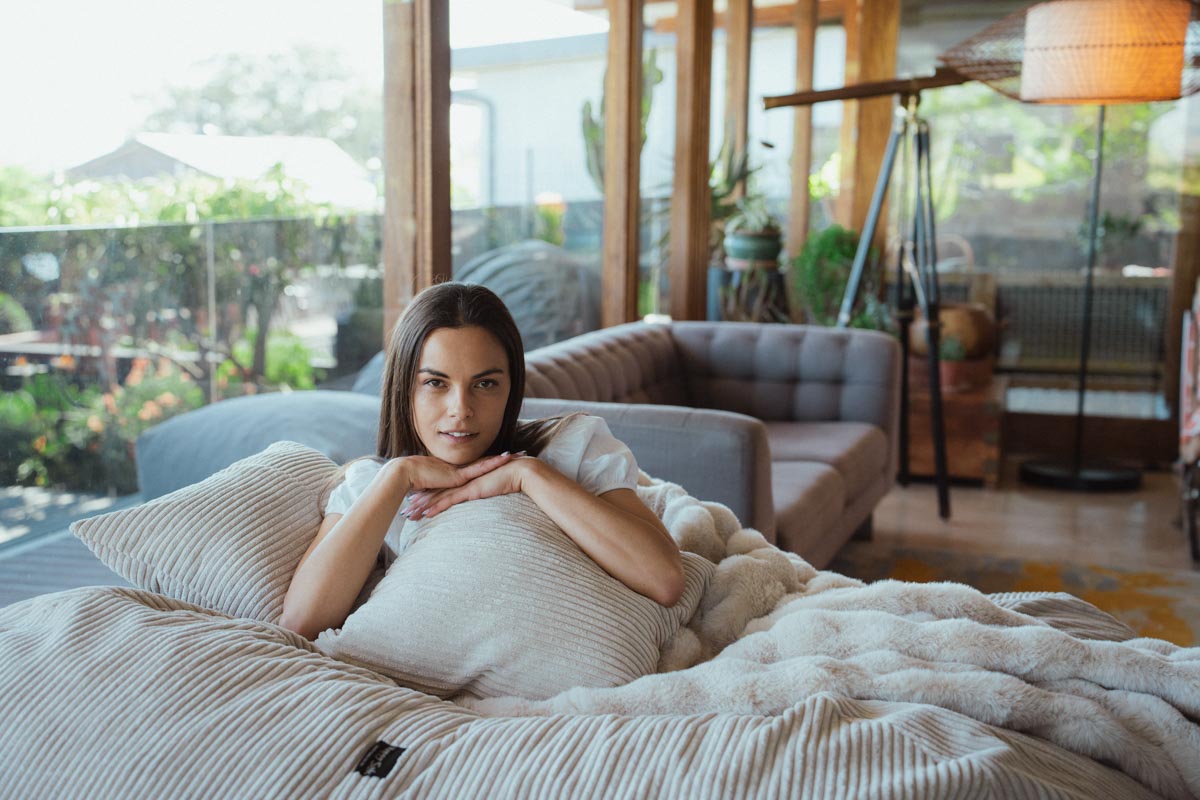 Woman lying on a couch with pillows and blanket in a cozy living room.
