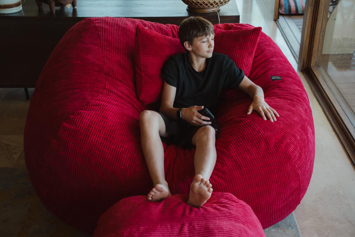 Child sitting on a large red bean bag chair indoors.