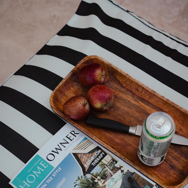Wooden tray with apples and a can on a black and white striped surface with a magazine underneath.