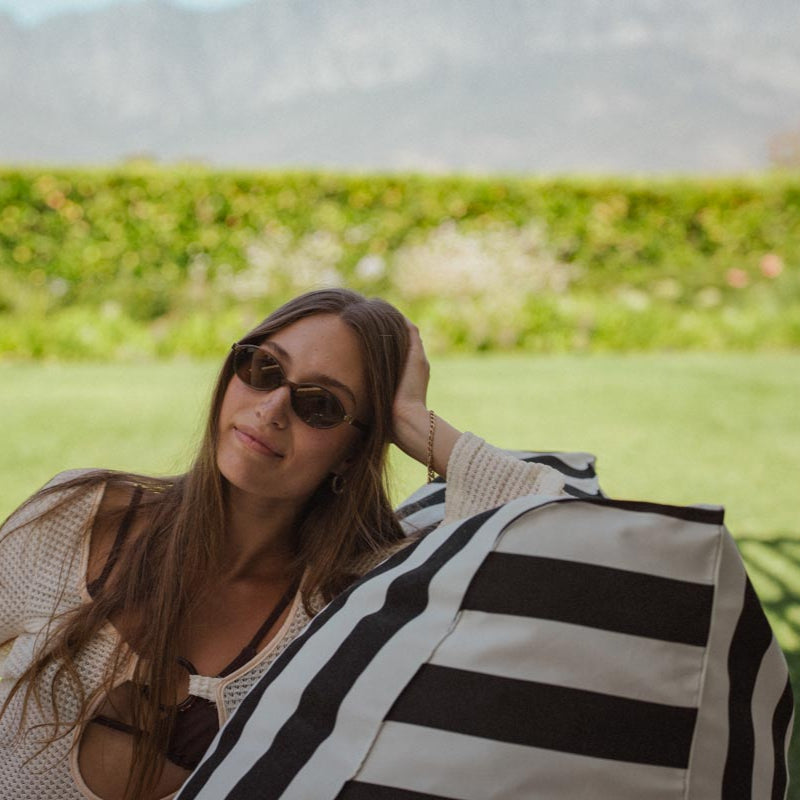 Woman sitting on a grassy field wearing sunglasses and a black and white striped cover-up.