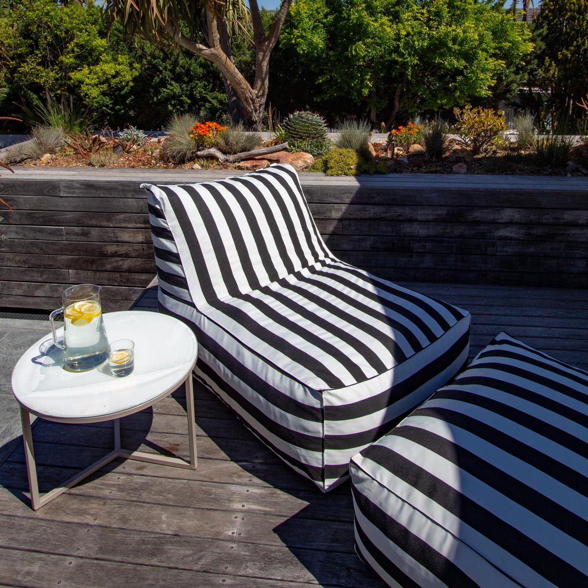 Black and white striped outdoor lounge chair on a wooden deck with a small table and drink.