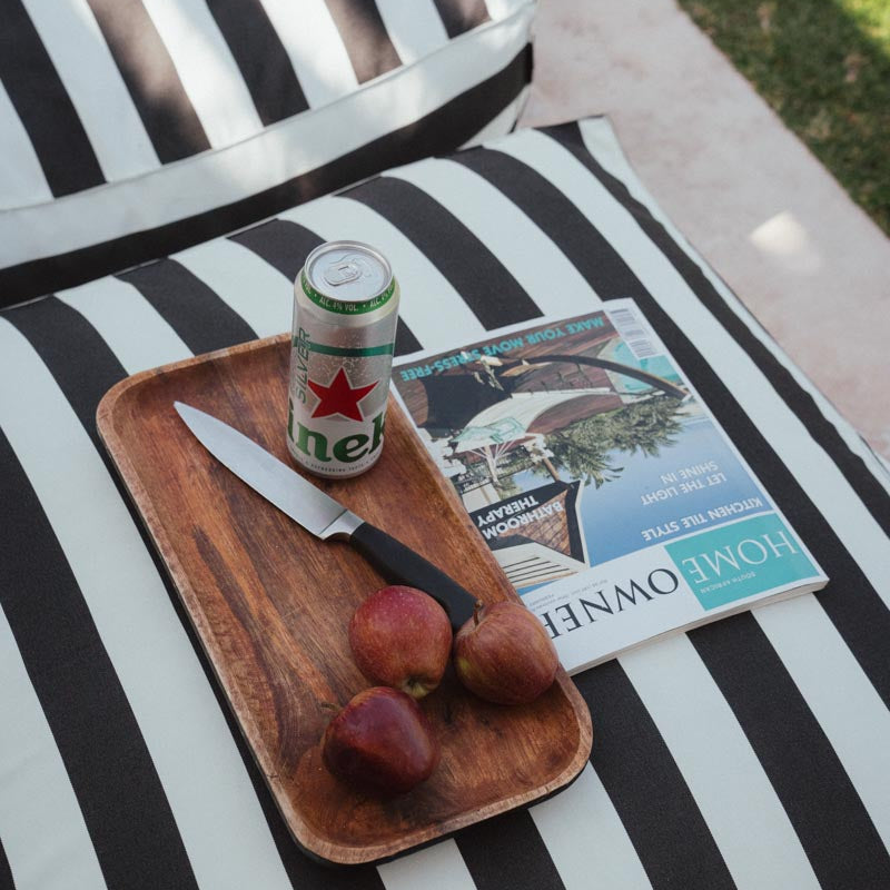 A black and white striped pool lounger chair cover displayed on a chair, with a magazine, tray with fruits, and a can on the tray.