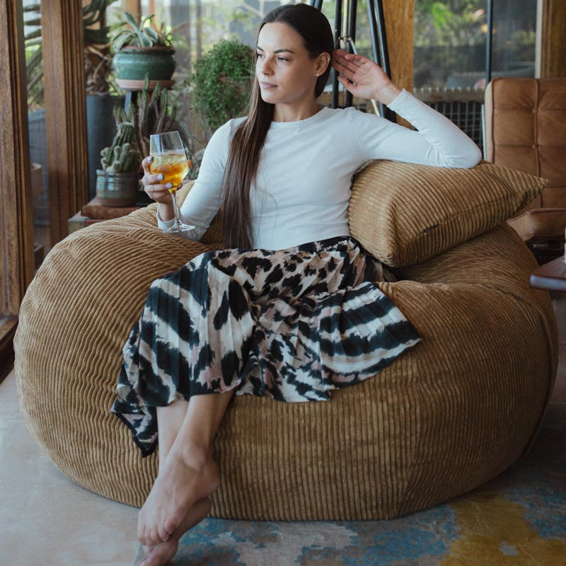 Woman sitting on a brown bean bag chair holding a glass of orange juice.