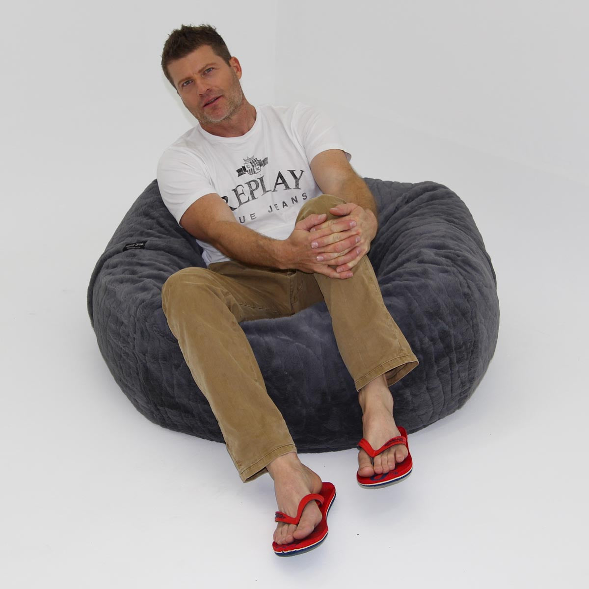 Man sitting on a gray bean bag chair wearing a Replay t-shirt and red sandals.