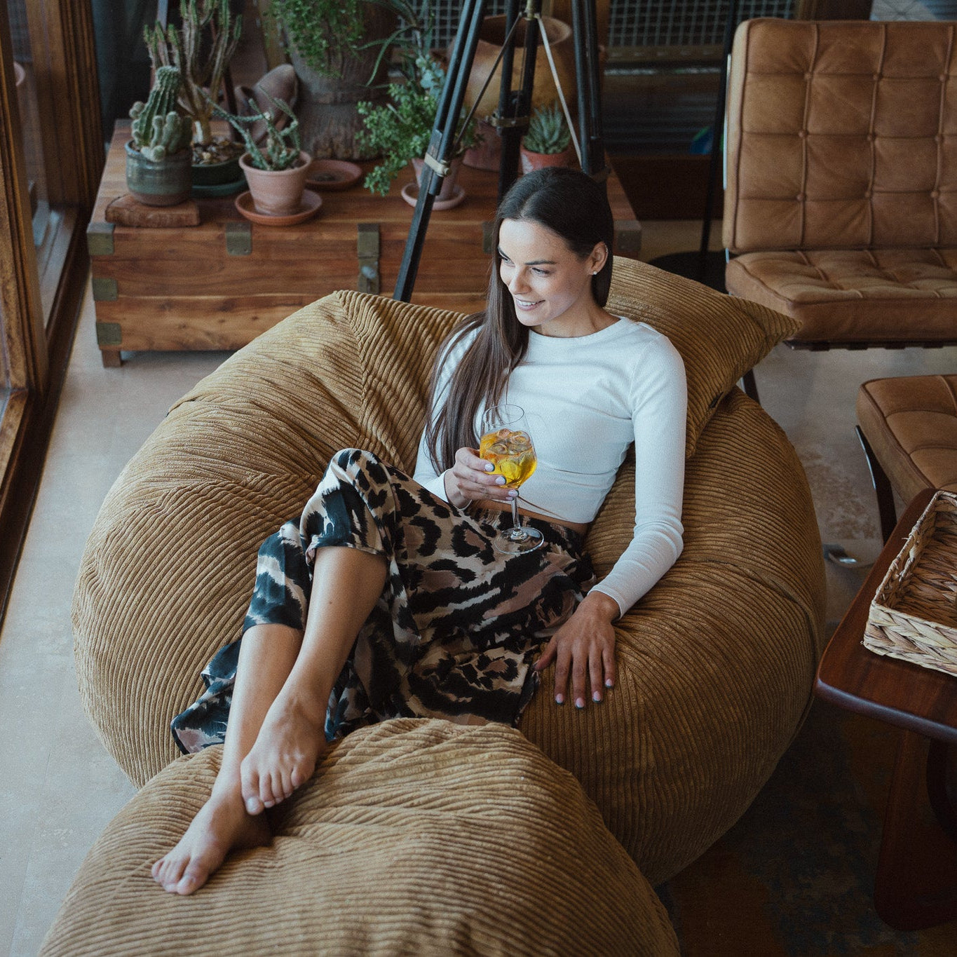 Woman sitting on a bean bag chair holding a glass of wine in a cozy living room.