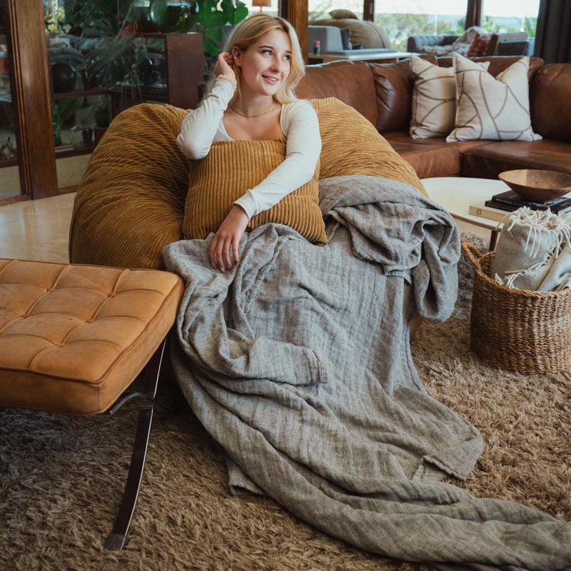 Woman sitting on a couch with a blanket, surrounded by a cozy living room.