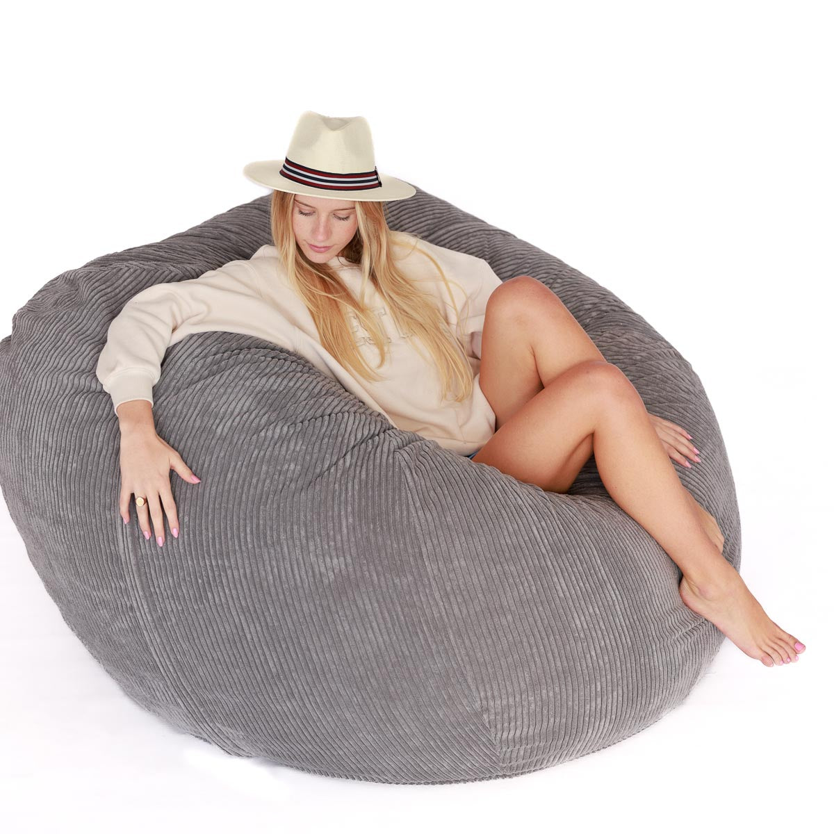 A person lounging on a large grey corduroy bean bag chair indoors.