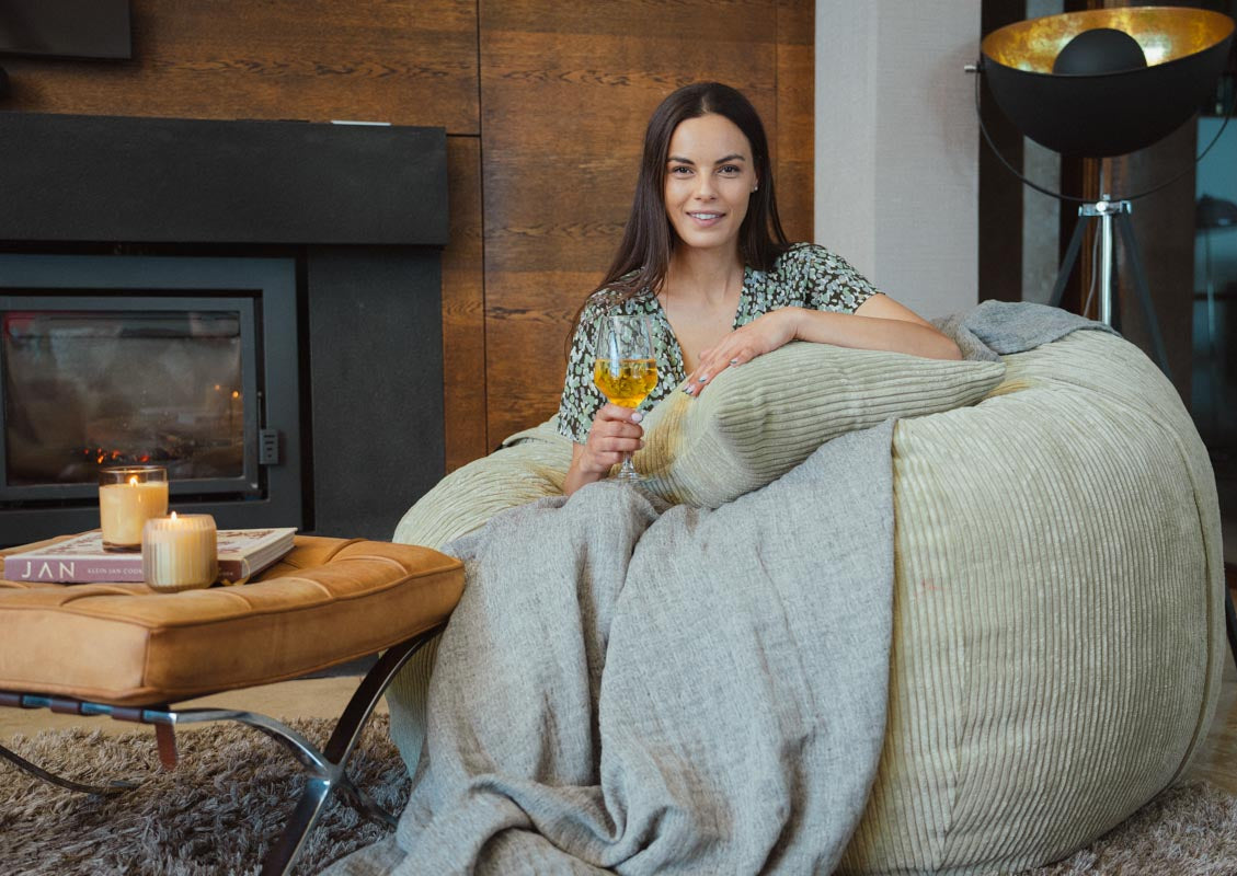 Woman sitting on a bean bag chair in a cozy living room with a fireplace and lamp.