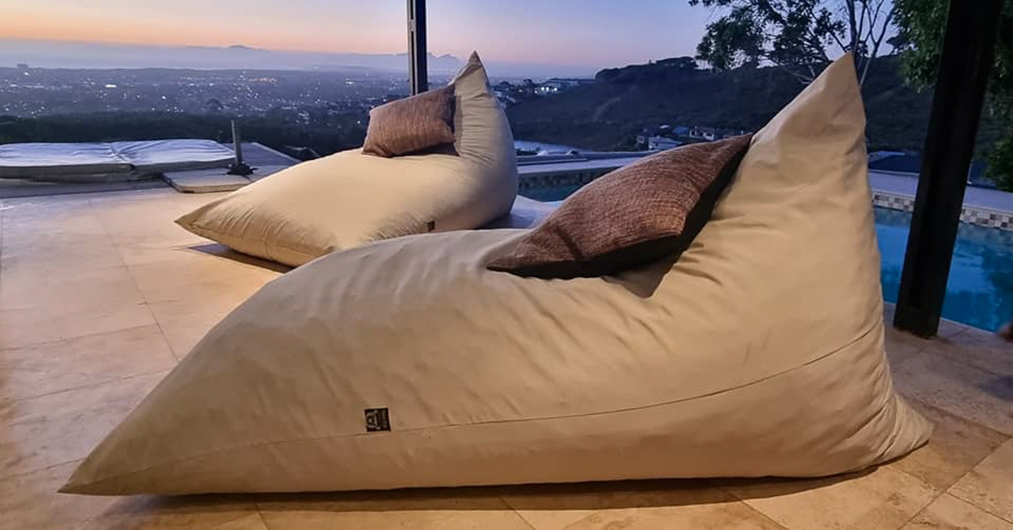 Beige bean bag chairs with brown cushions on a patio with a scenic view.