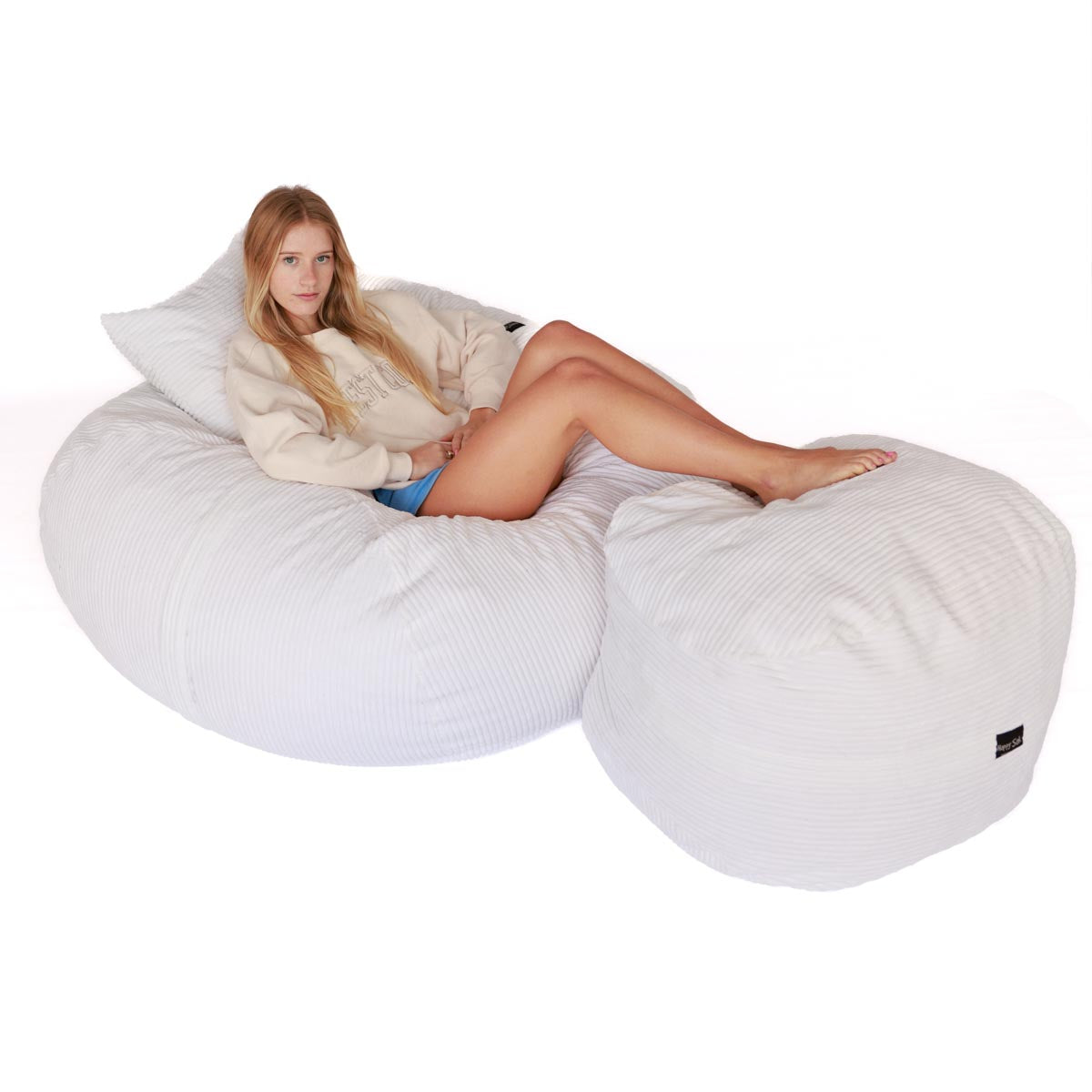 a person sitting on a white corduroy bean bag with a scatter cushion and ottoman