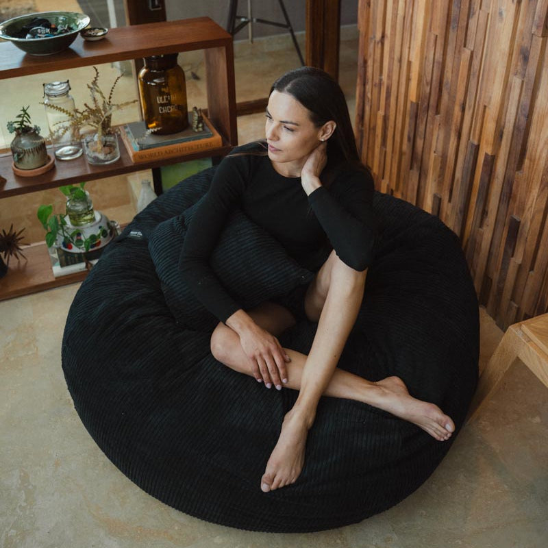 Woman sitting on a black bean bag chair in a room with wooden shelves and decor.