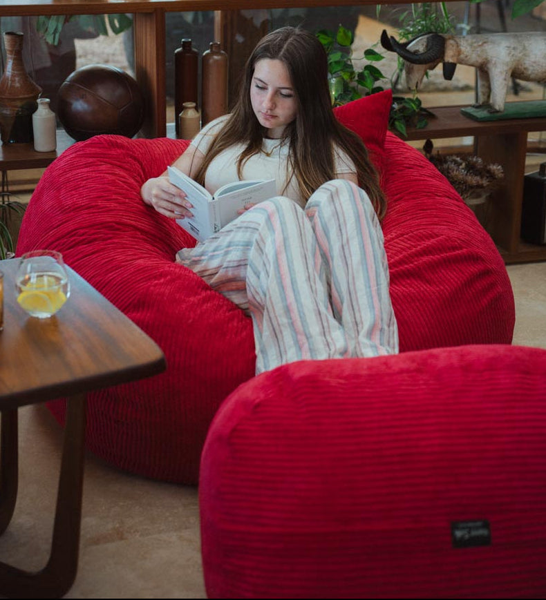 Woman reading a book on a red bean bag chair in a cozy room.