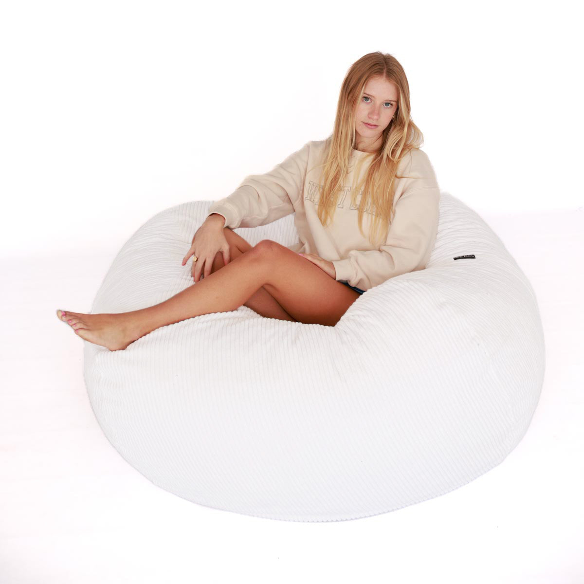 Woman sitting on a white bean bag chair against a white background