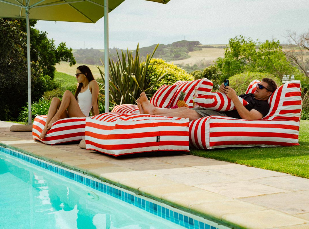 Two people relaxing on striped bean bags by a poolside.