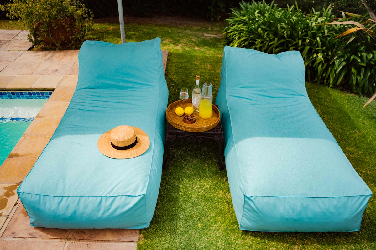 Two turquoise lounge chairs by a pool with a small table and items on a grassy area.