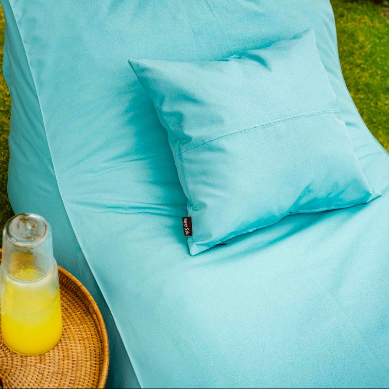 Turquoise bean bag chair with a small table holding drinks and lemons on grass.