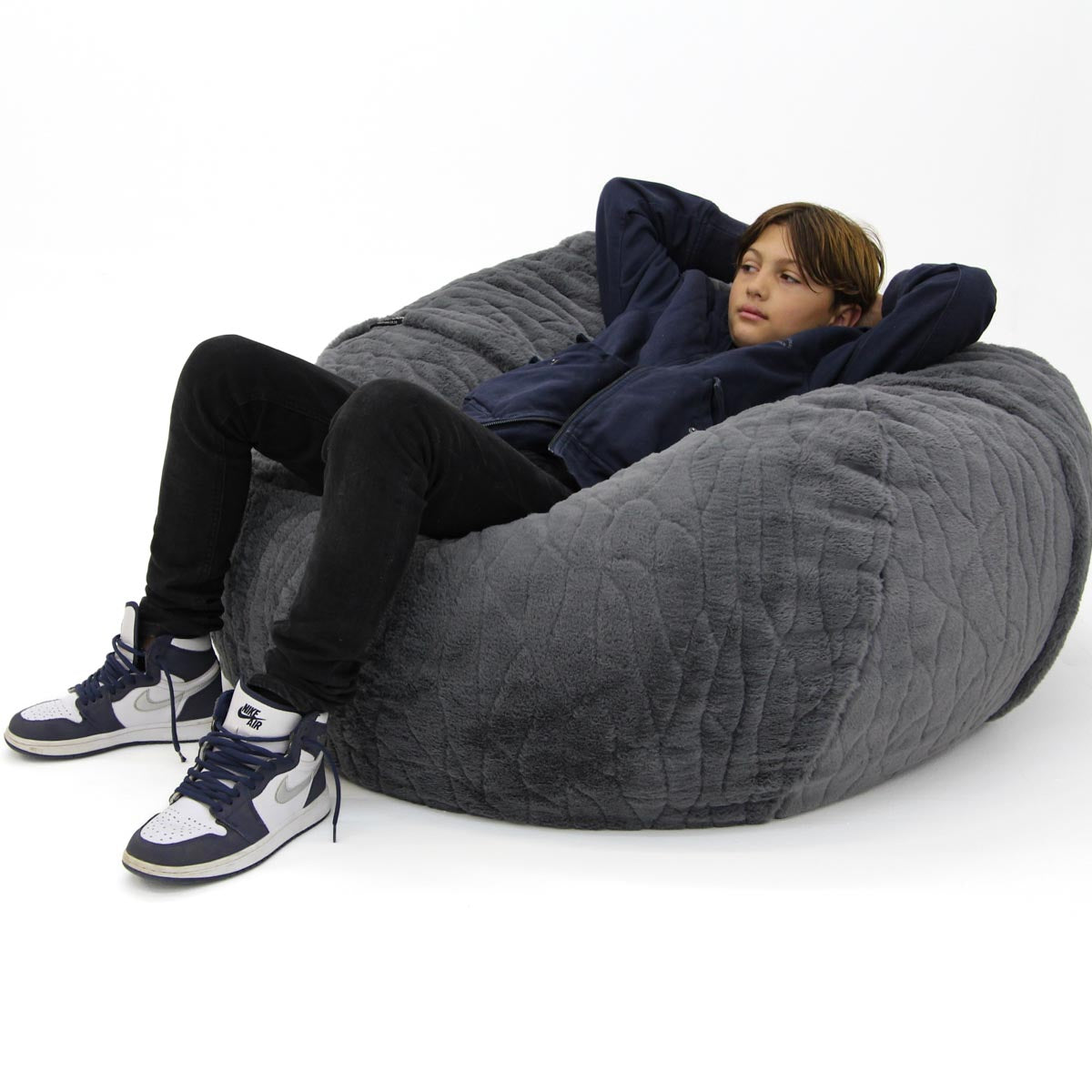 Person sitting on a large gray bean bag chair against a white background